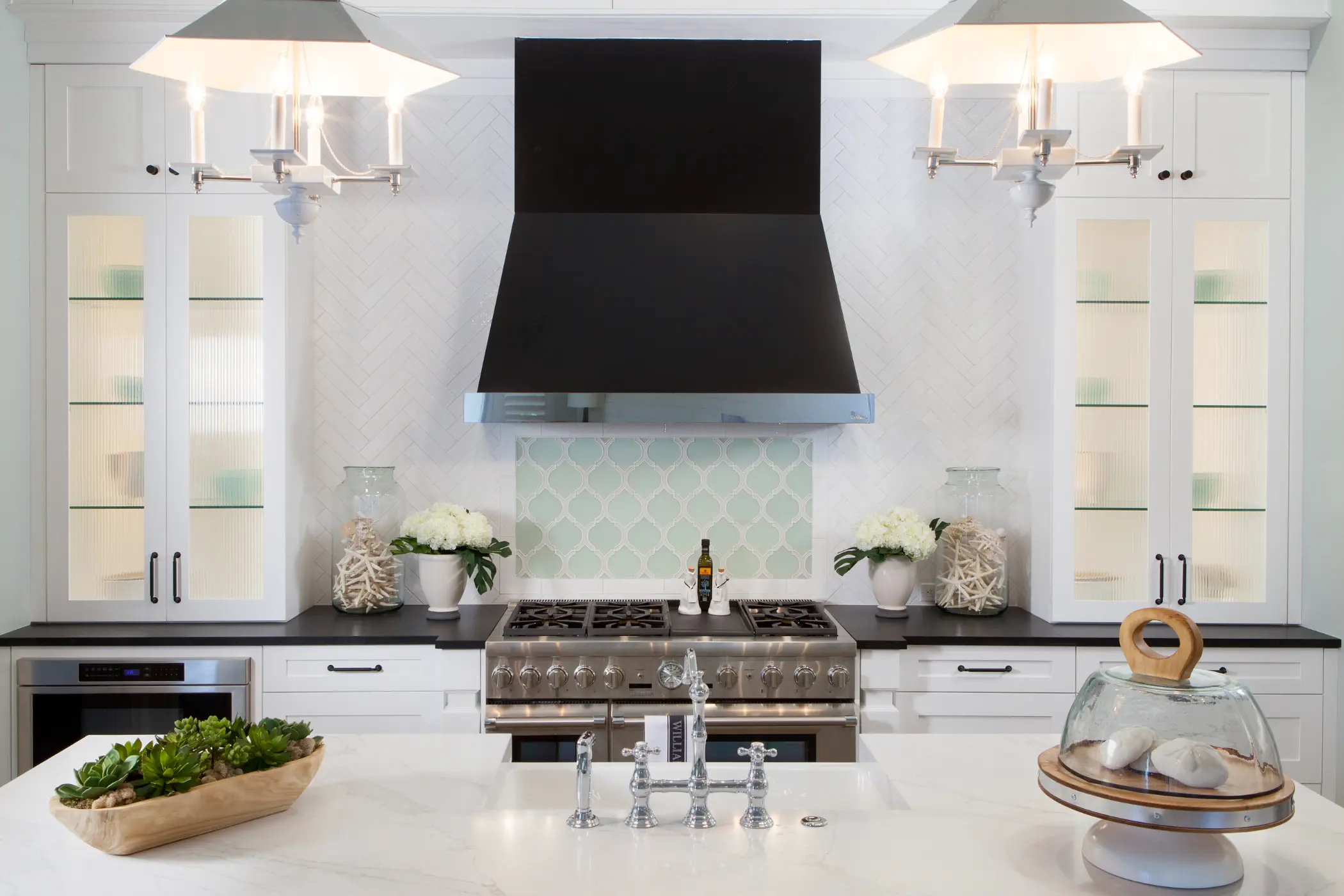Modern kitchen with a large black range hood above a sleek stove and marble island countertop.