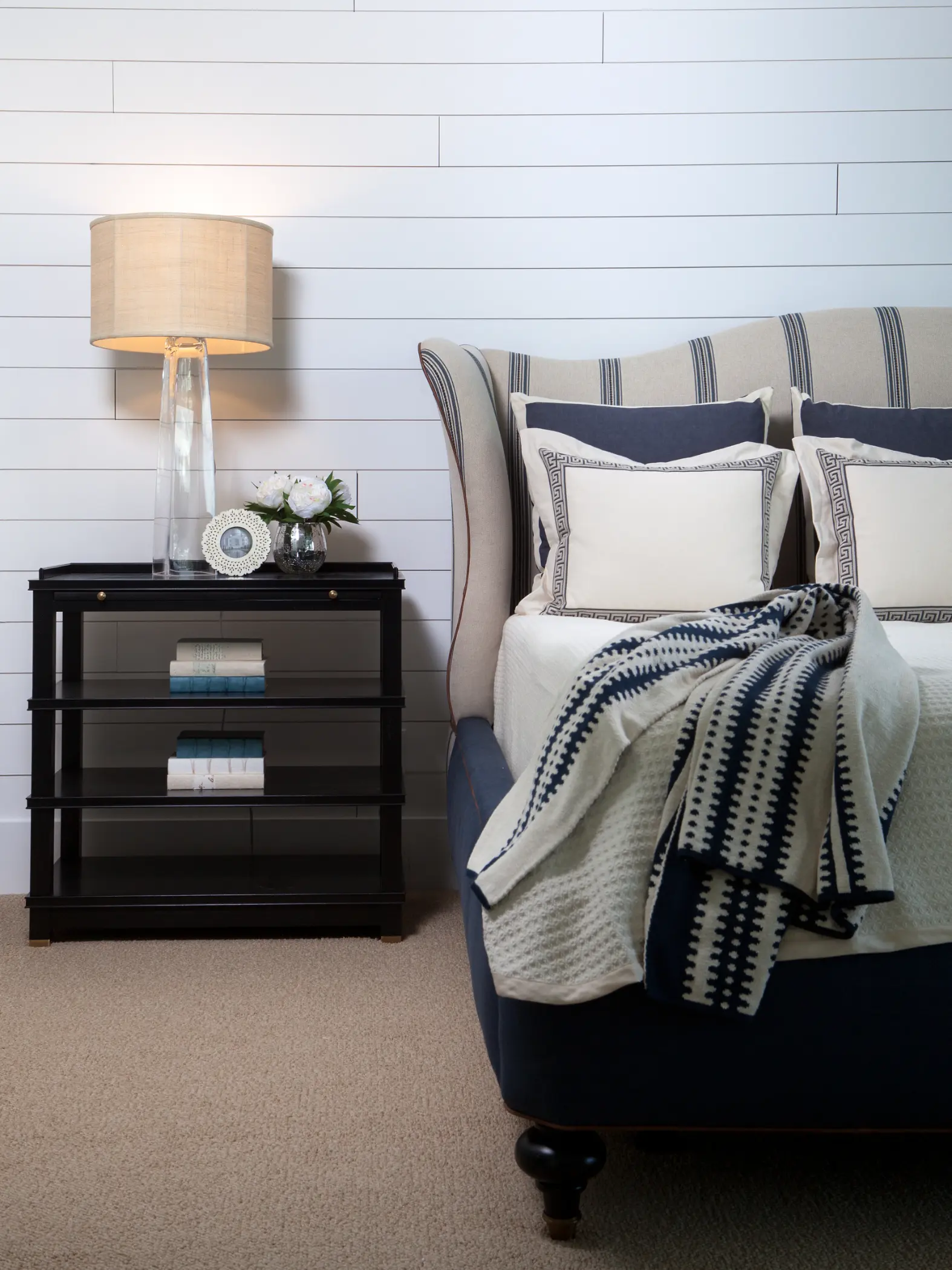 Bed with patterned pillows and blanket next to a nightstand with a lamp and small decor.