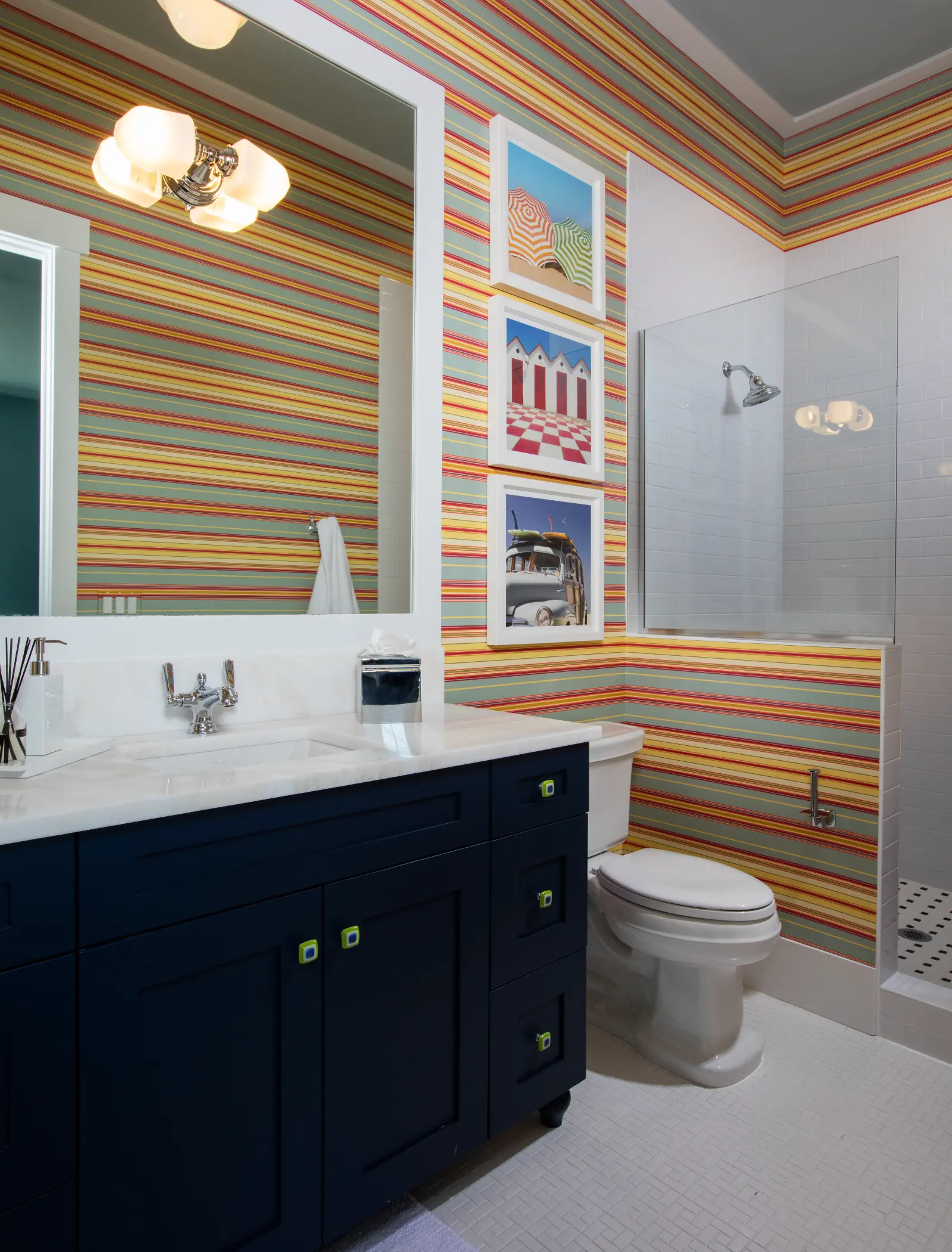 Bathroom with a navy blue vanity, striped wallpaper, and framed pictures on the wall.