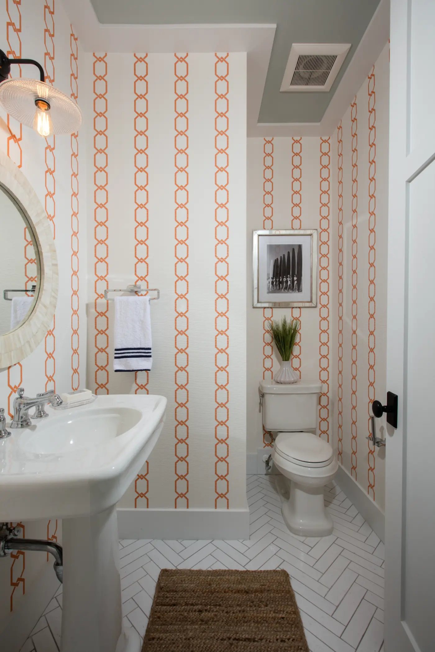Bathroom with a white sink, circular mirror, toilet, and orange patterned wallpaper.