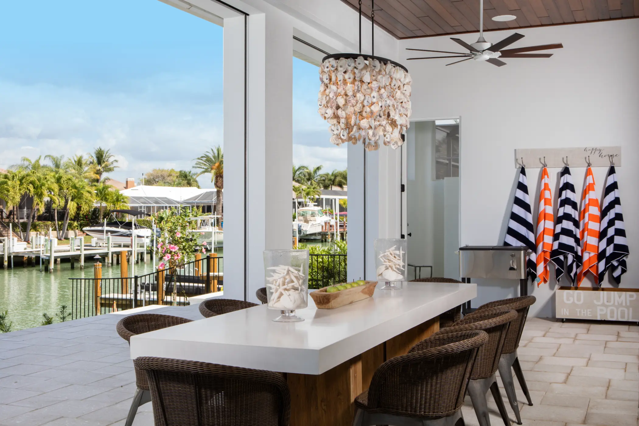 Outdoor dining area with a long table, shell chandelier, and view of water and docks.