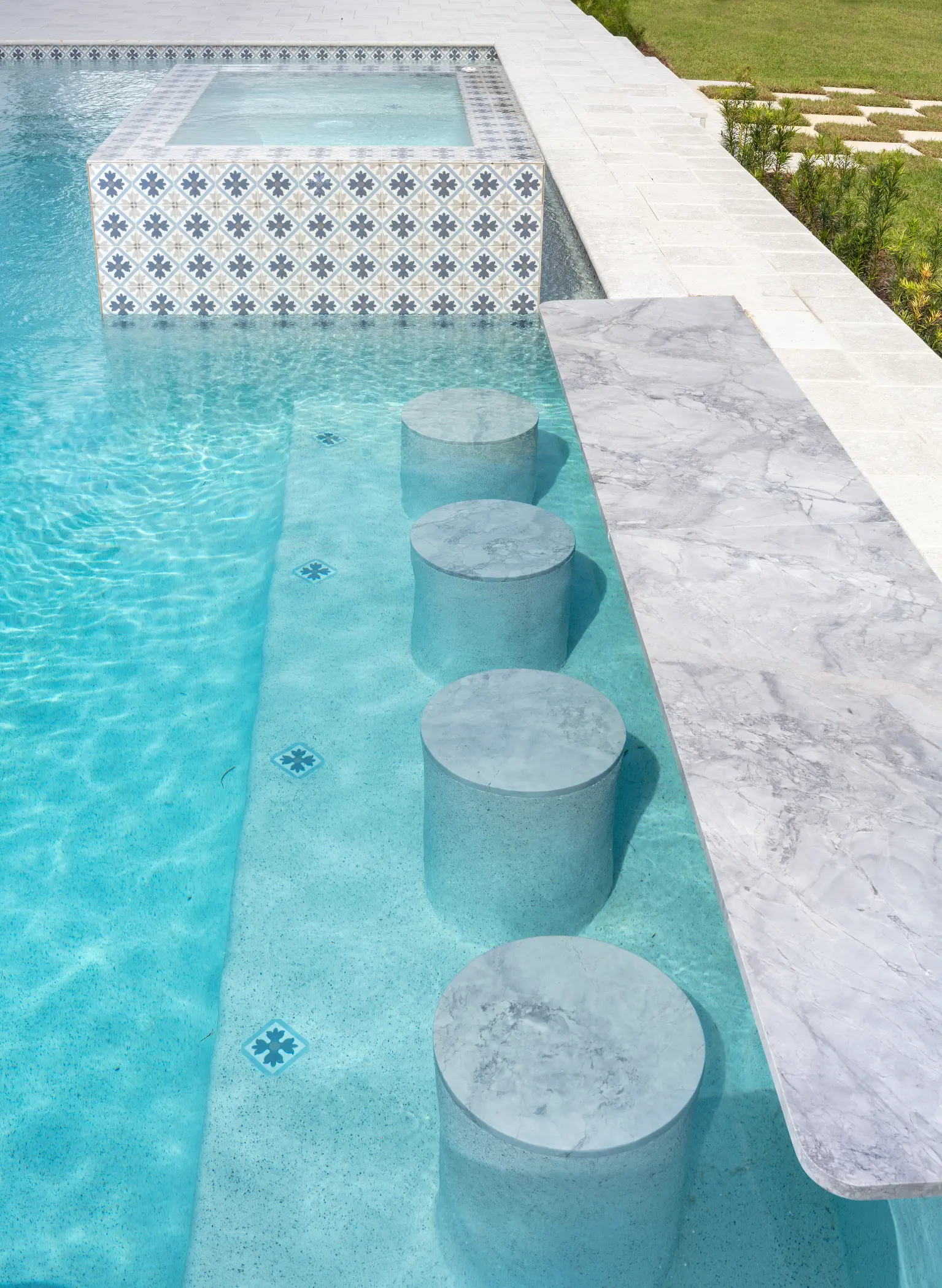Stools are submerged in a pool alongside a marble-topped bar, creating a swim-up seating area.