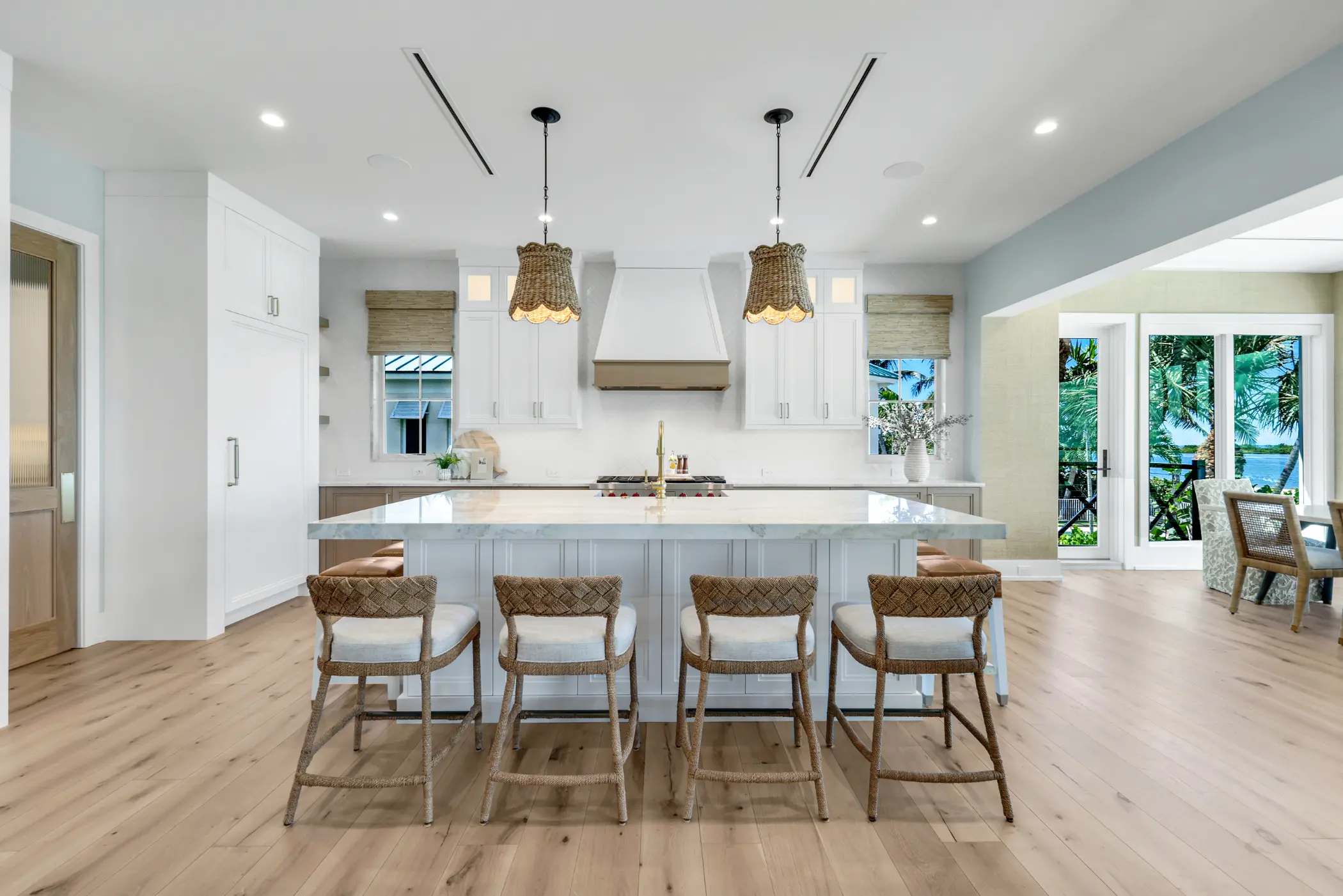 A modern kitchen with an island, four chairs, pendant lights, and a large window view.