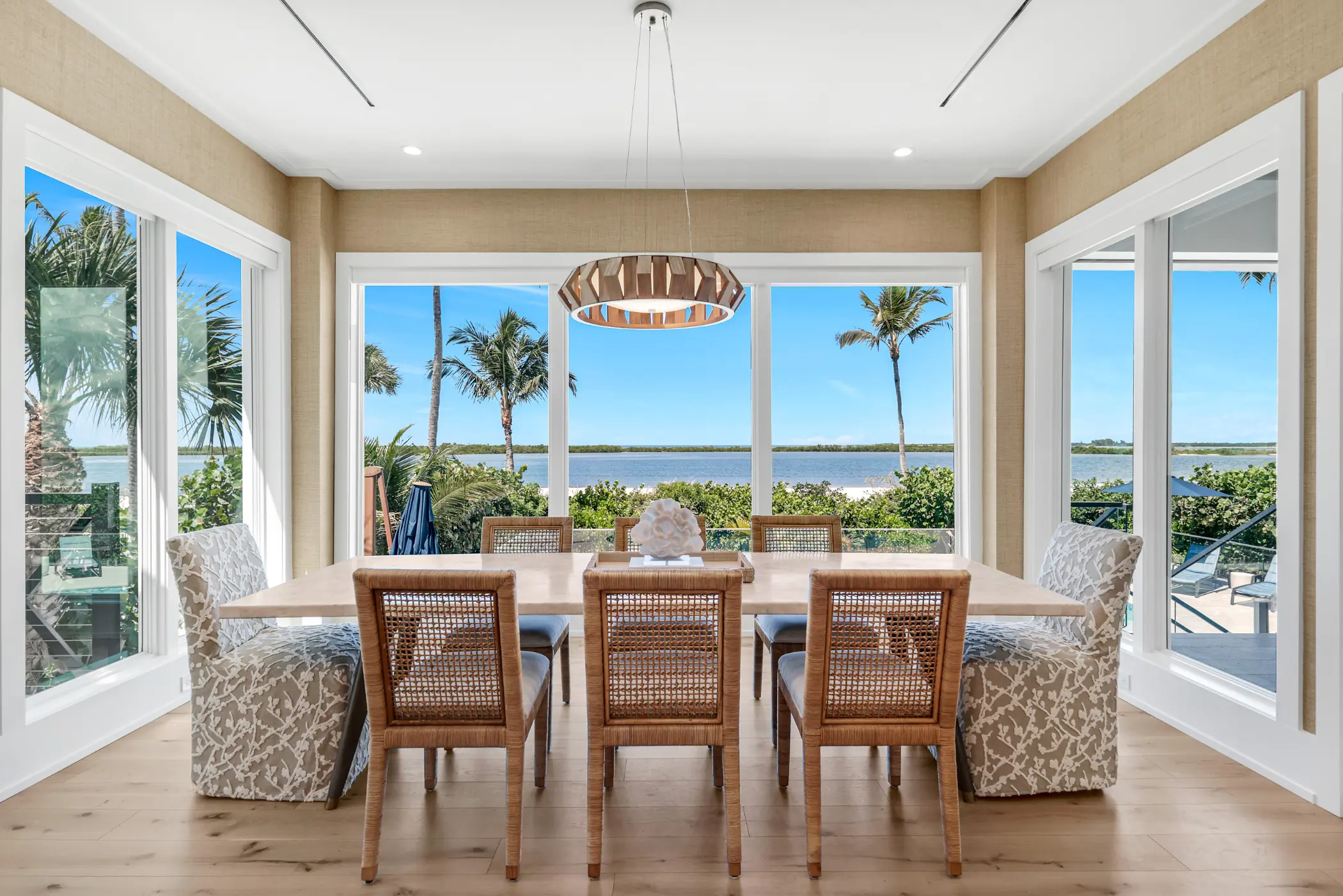 Dining room with a large table and eight chairs, overlooking a view of palm trees and a body of water.