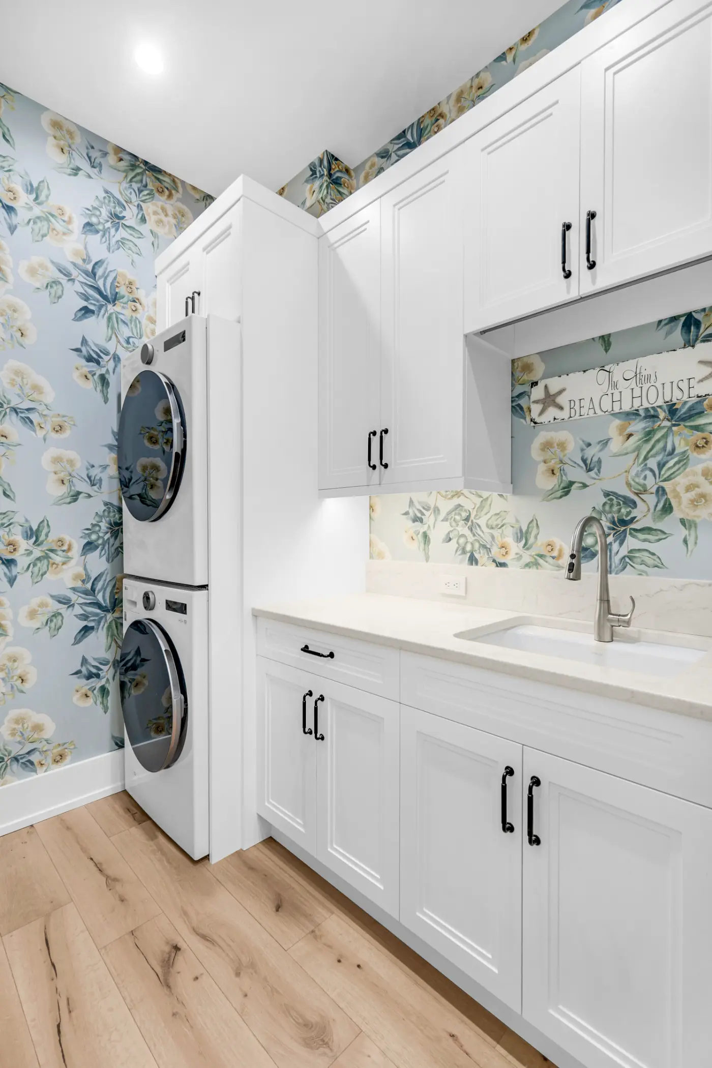 A laundry room with a stacked washer and dryer next to a sink and white cabinets.