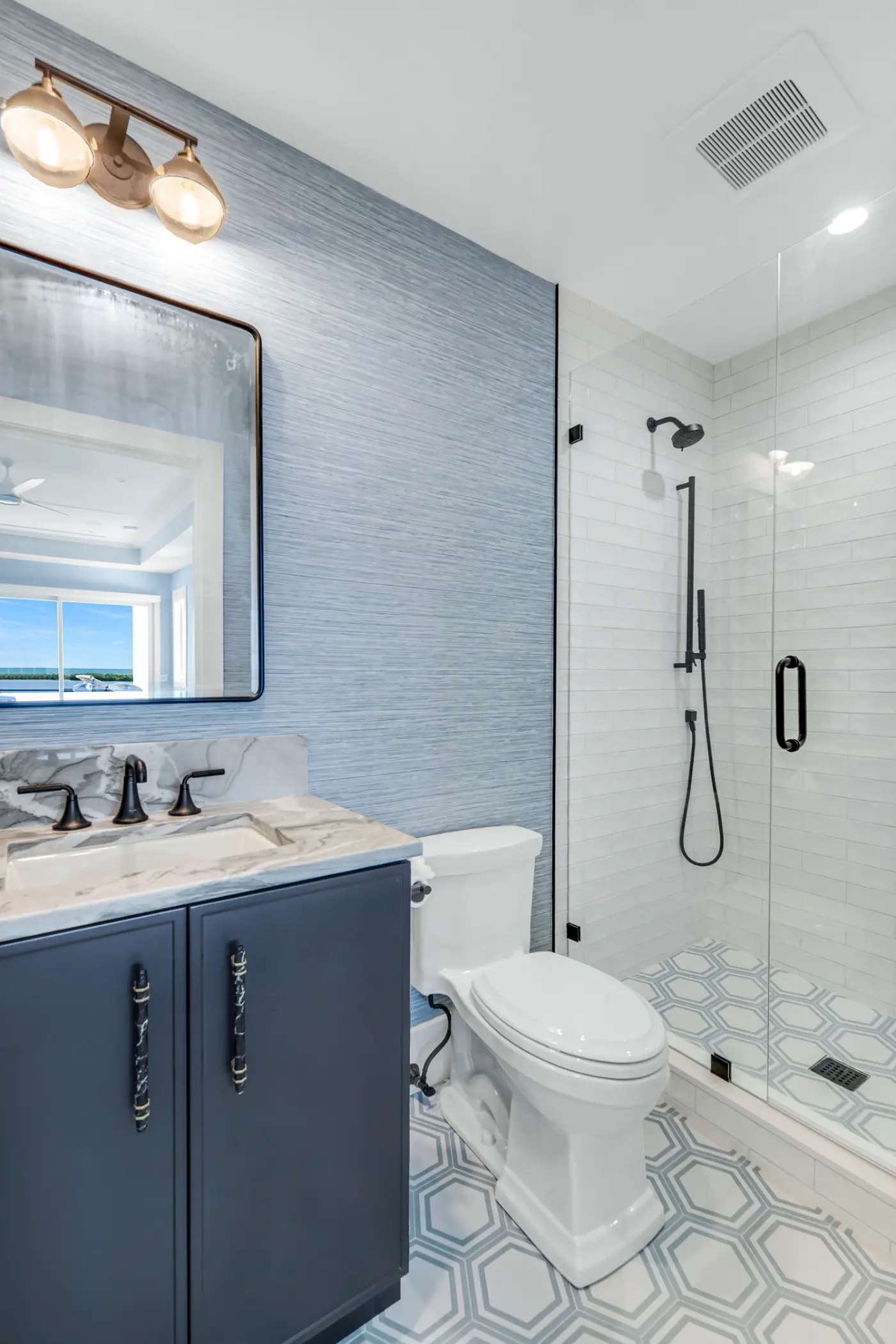 Bright bathroom with a blue vanity, white toilet, and glass-enclosed shower with black fixtures.