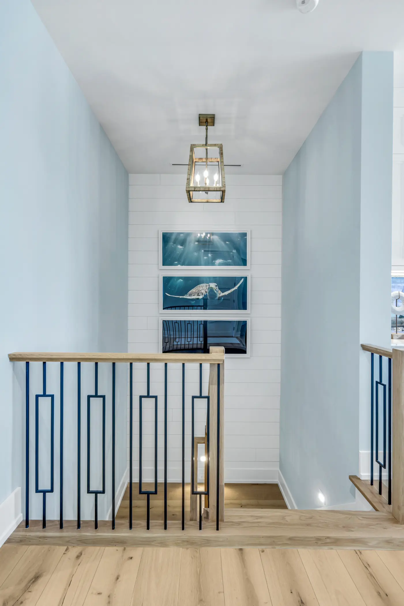 A stairway with light blue walls, a nautical-themed painting, and a wooden handrail.