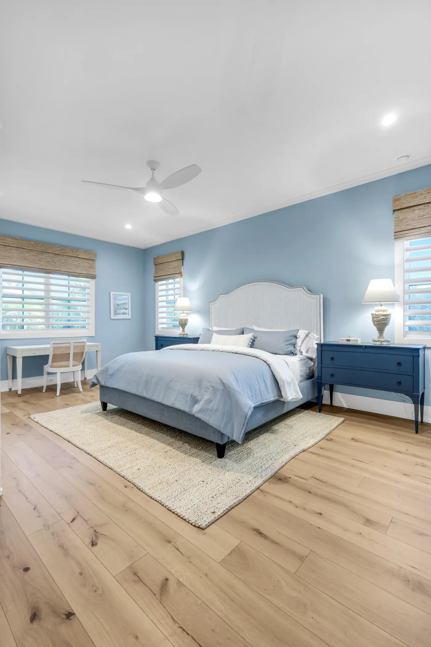 A bedroom with a large bed, two blue nightstands, and a writing desk by the window.