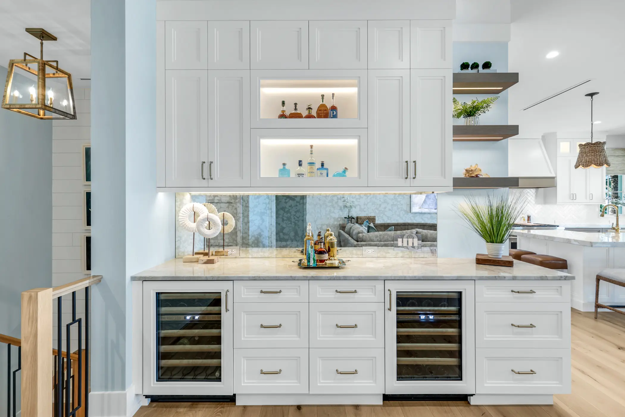 A modern kitchen with a white cabinet featuring built-in wine coolers and shelves displaying bottles.