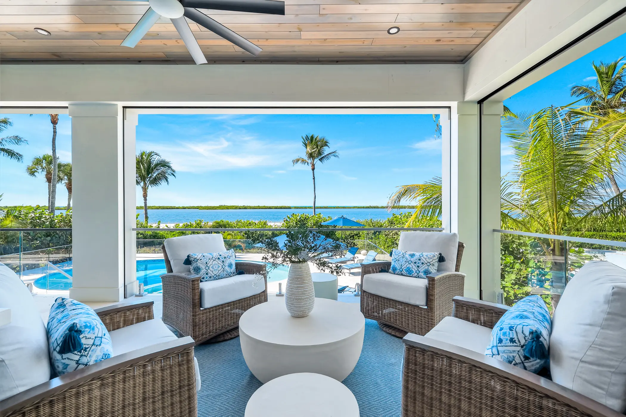 Outdoor seating area with wicker chairs and a round table, overlooking a pool and tropical scenery.