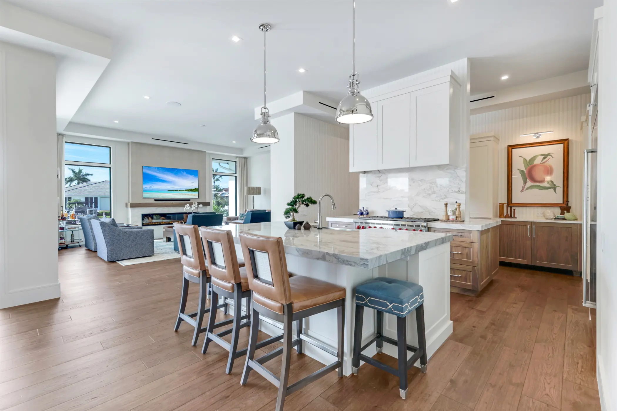 A modern kitchen with a marble island, three chairs, and a view of the living room.