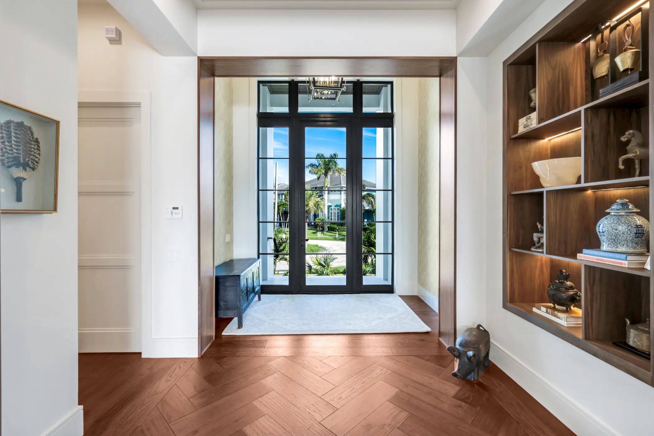 A foyer with wooden floors, a bookshelf, and glass doors leading to a garden view outside.