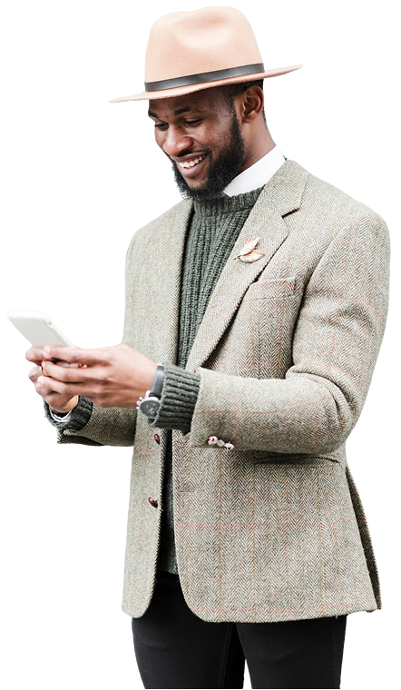 Smiling man wearing a beige fedora hat, gray tweed blazer, and dark sweater, looking at and holding a smartphone.
