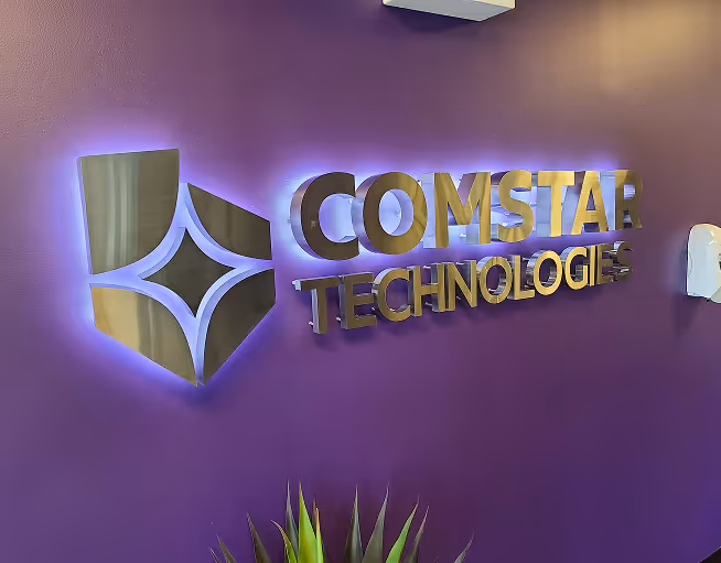 Illuminated lobby wall sign with dimensional gold letters for Comstar Technologies on purple background, featuring LED halo backlighting