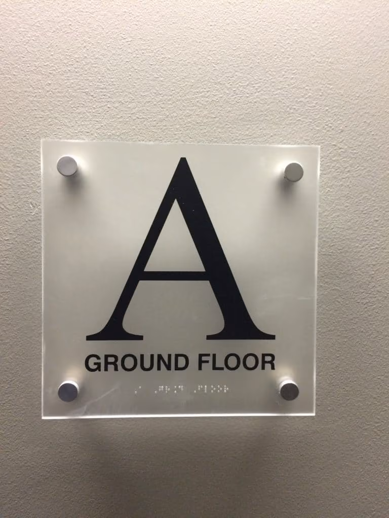 ADA acrylic sign with braille mounted with four aluminum standoffs