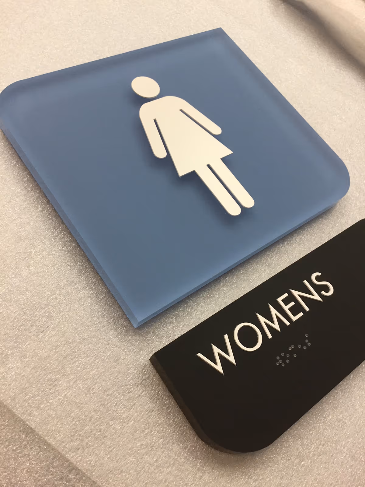 Custom ADA compliant women’s restroom sign with tactile lettering, braille, and modern acrylic design