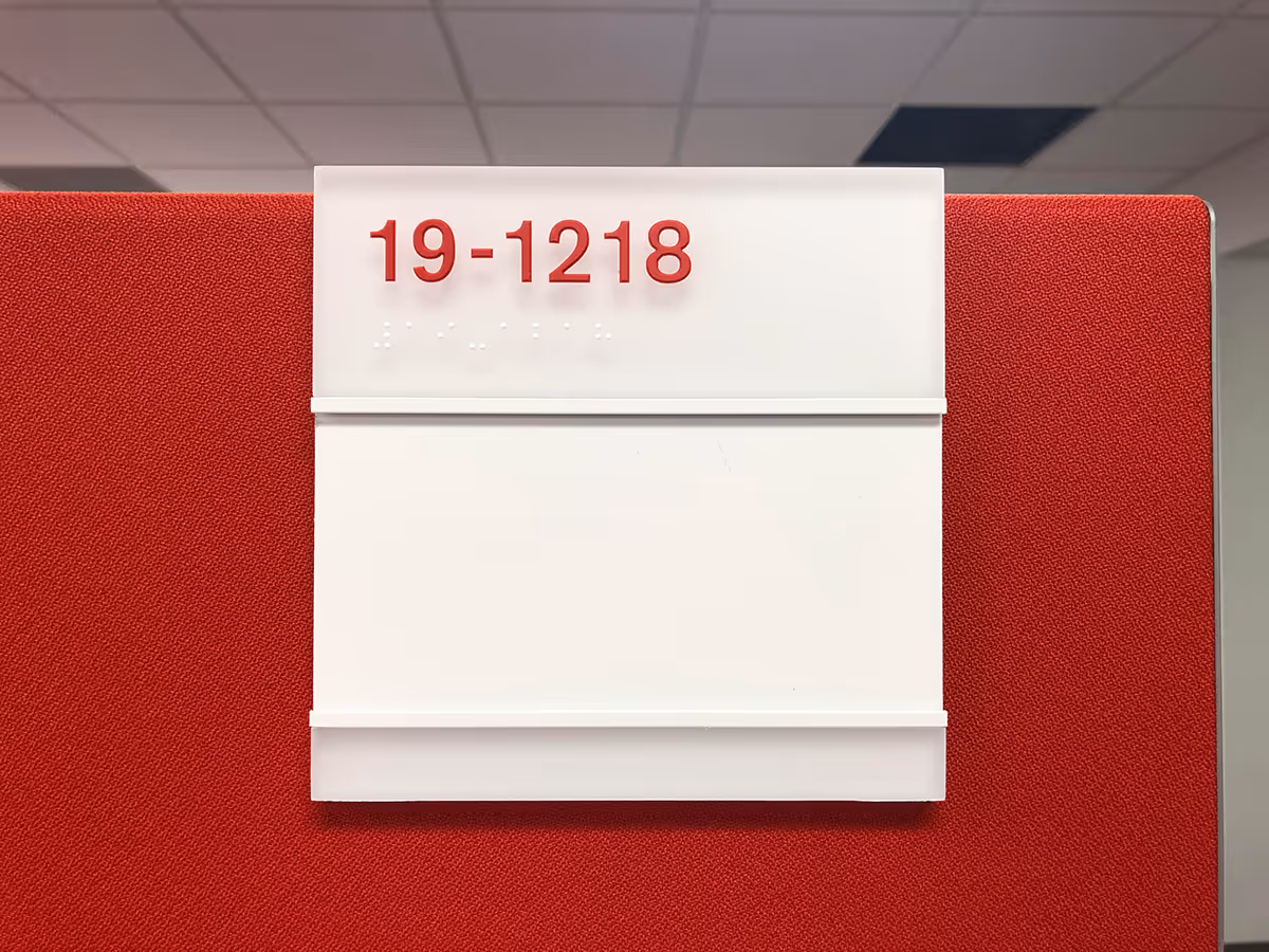 Custom ADA office room number sign with raised red lettering and braille, mounted on a red fabric wall panel