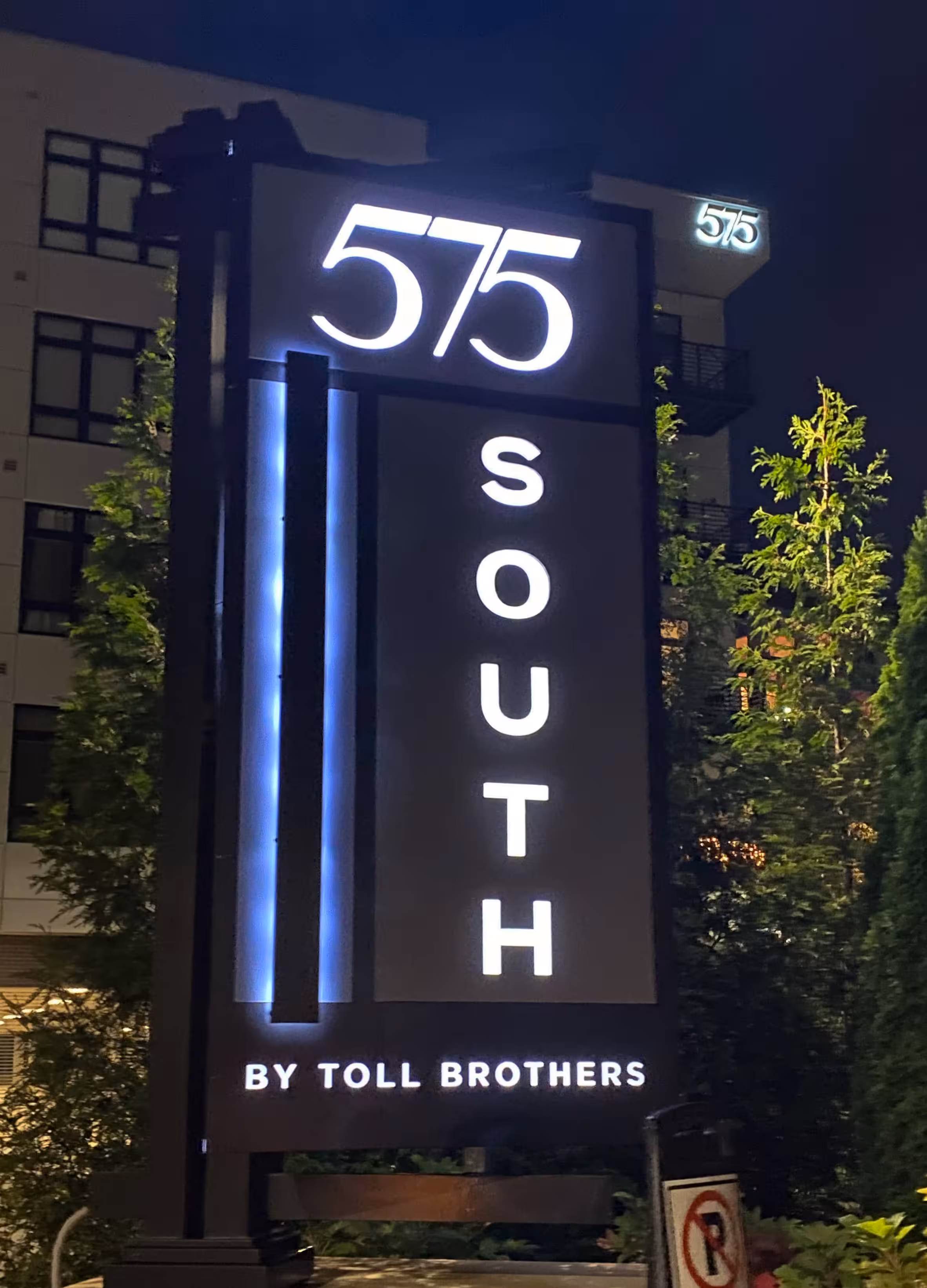 Illuminated monument sign reading ‘575 South by Toll Brothers’ with vertical lighting accents, photographed at night.