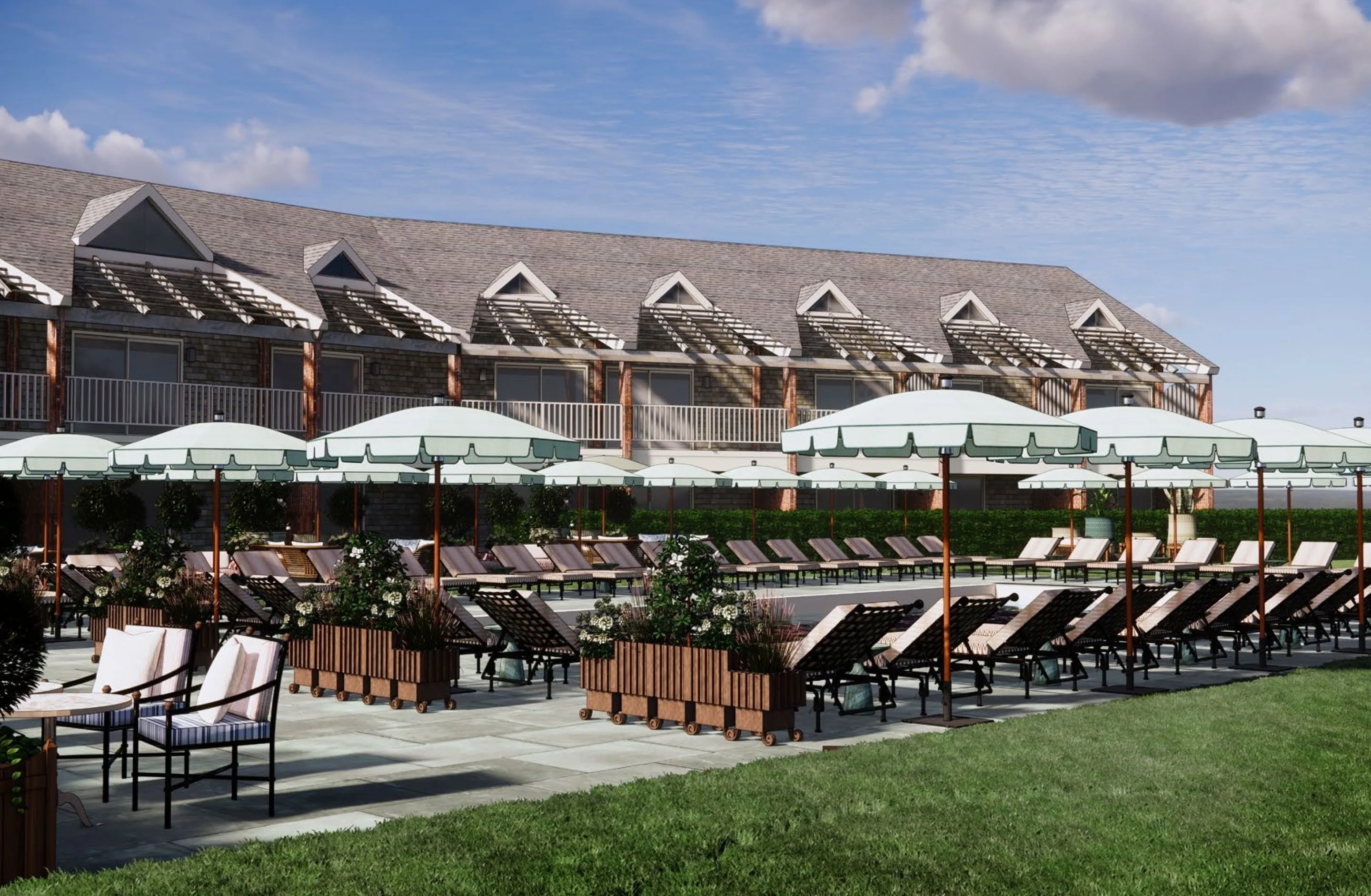 Outdoor pool area with lounge chairs, umbrellas, and planters in front of a two-story building under a partly cloudy sky.