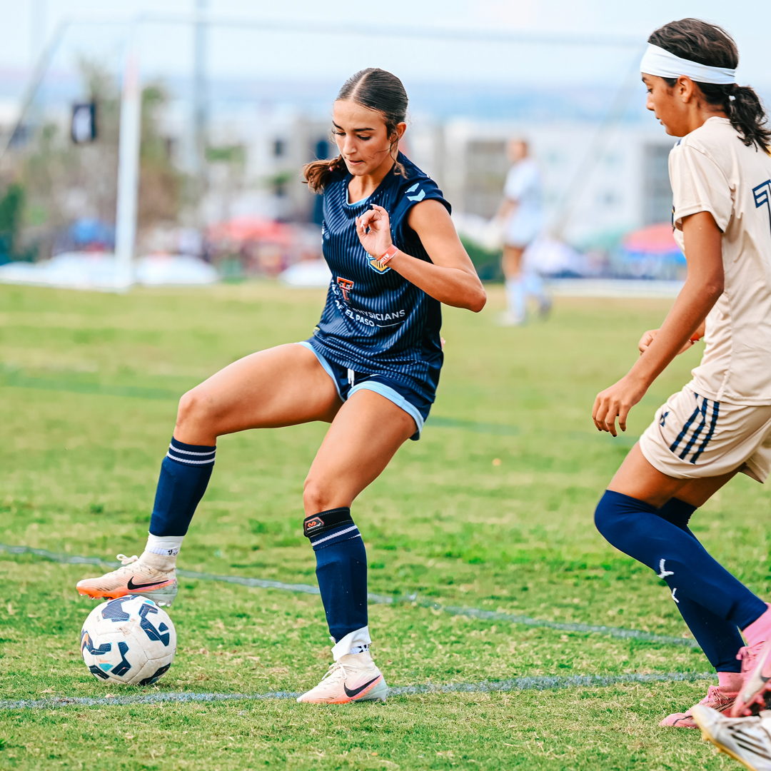 A female soccer player shielding the ball under pressure.