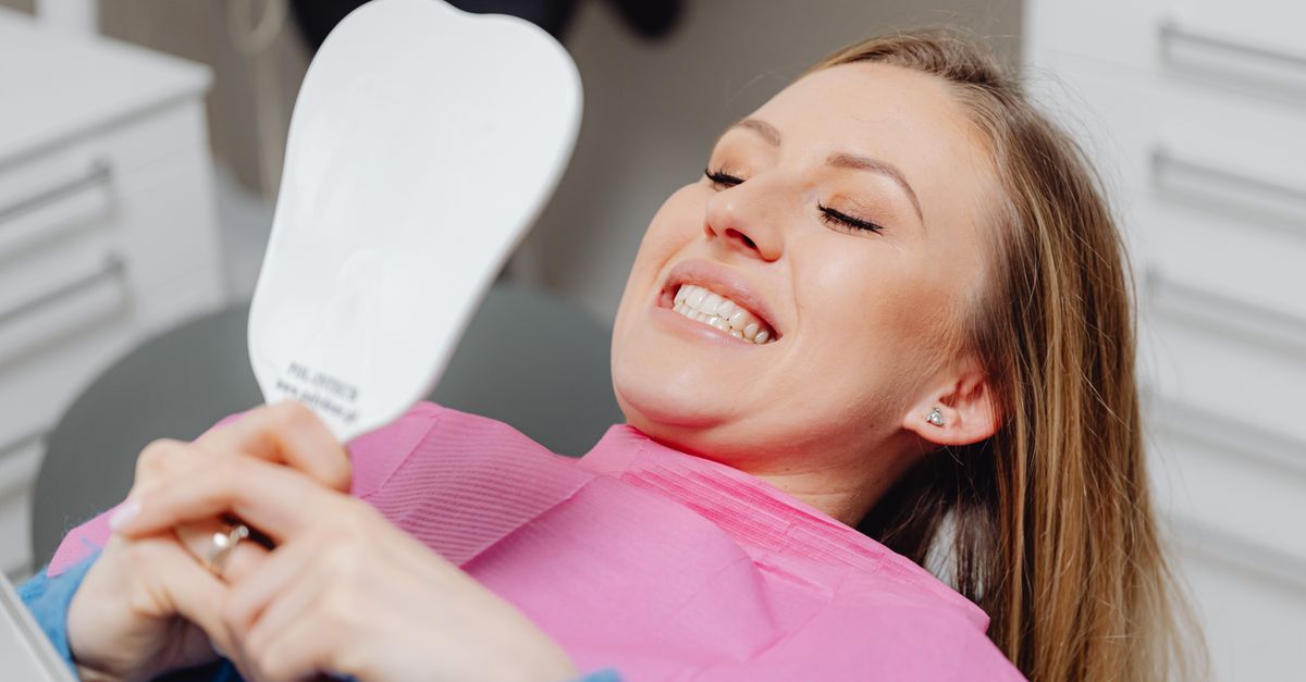 Woman in a dental chair checking her smile in a hand mirror