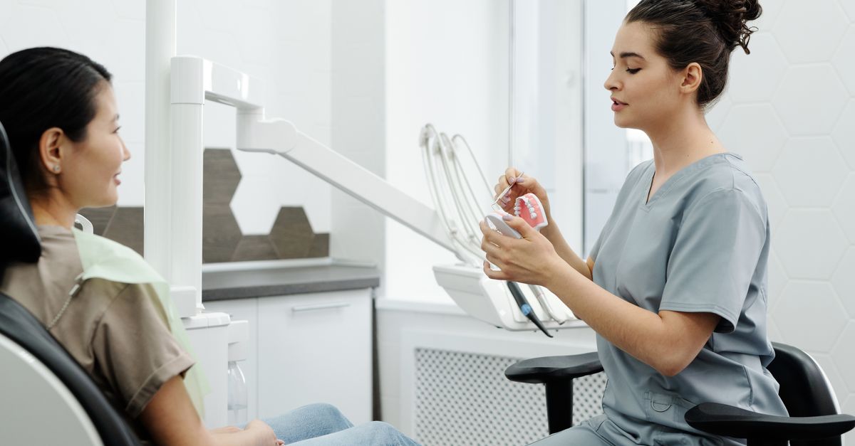 Dentist explaining a treatment option with a tooth model to a woman in the dental chair