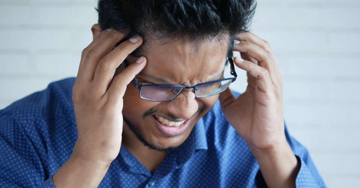 Man in glasses pressing his temples with both hands from a headache