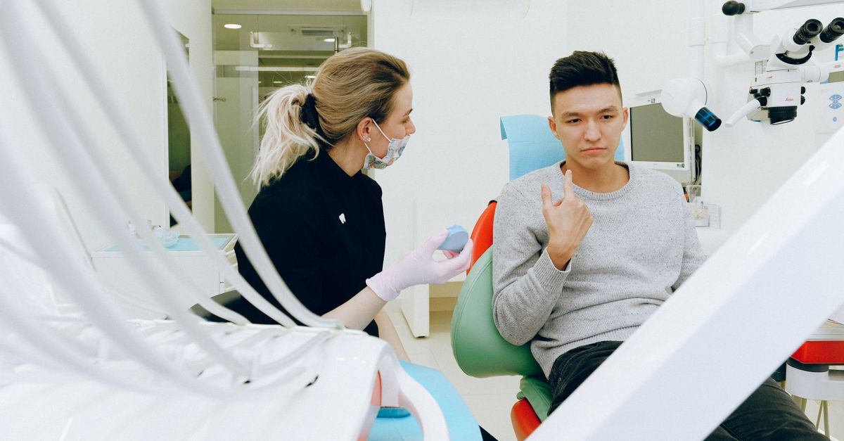 Man in a dental chair pointing to his jaw while talking with a dentist