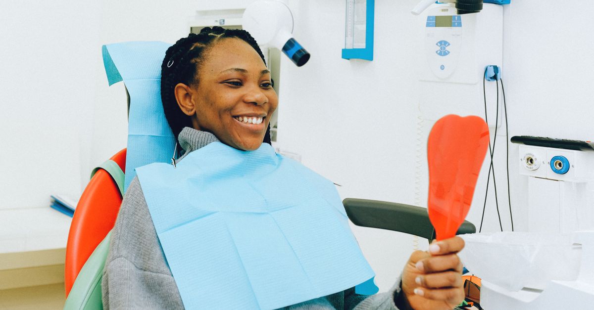 Smiling woman holding a hand mirror in a dental chair during a check-up