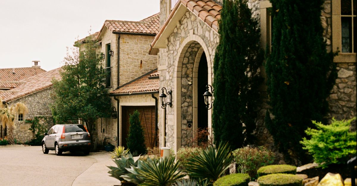 Stone house with trees and a gated entry on a residential street in Dallas