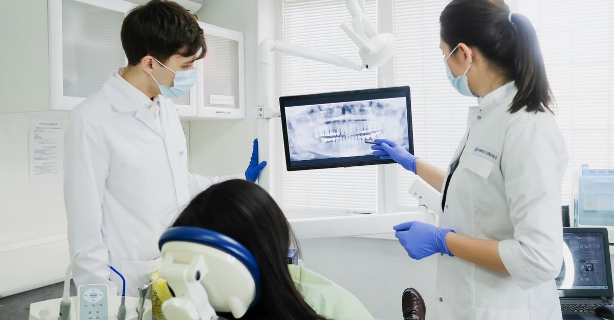 Dentist pointing to a dental X-ray on a screen while a patient sits in the chair