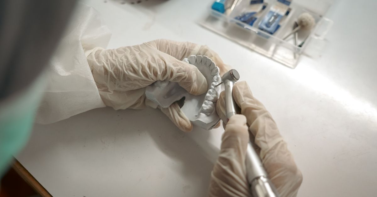 Gloved hands shaping dental work on a model in a dental lab