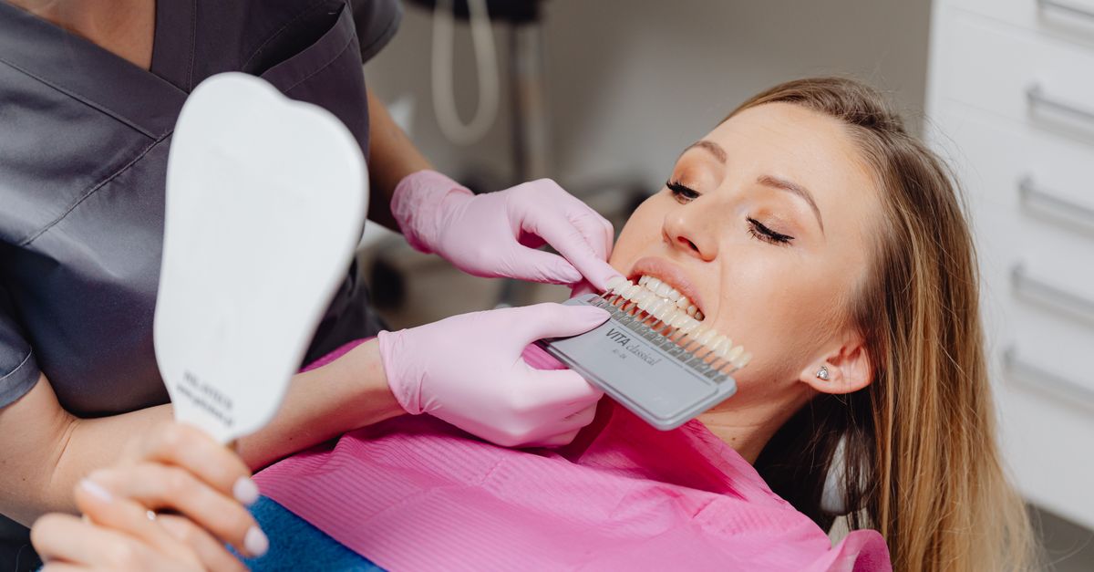 Dentist holding a tooth color guide next to a woman's smile in the dental chair