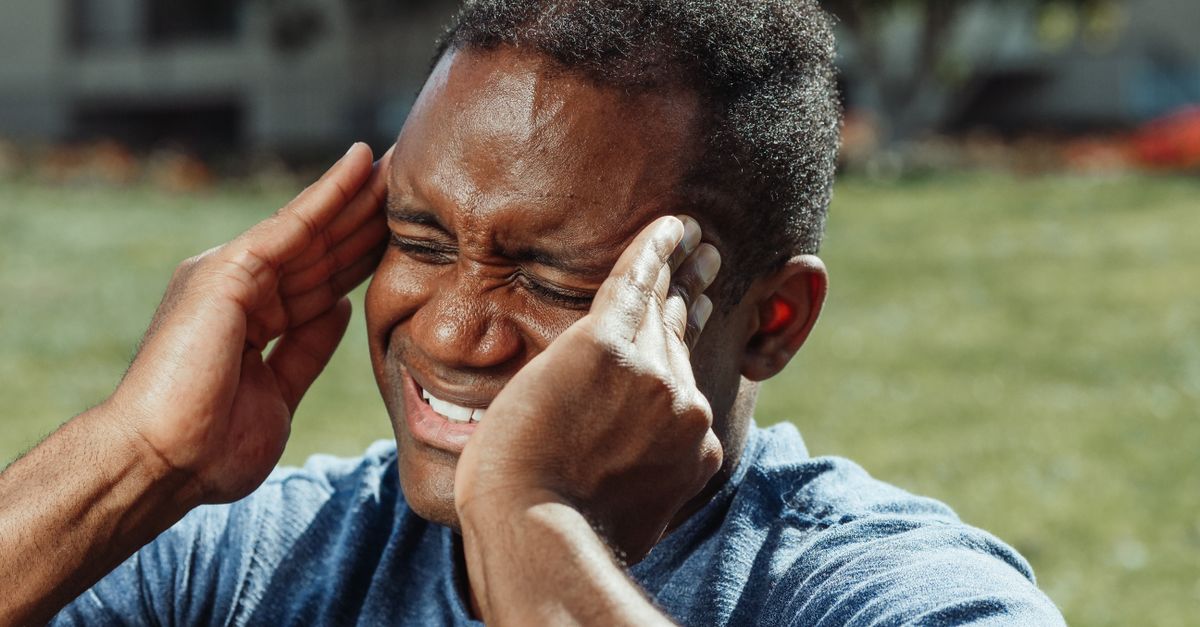 Man outdoors pressing his temples with a headache