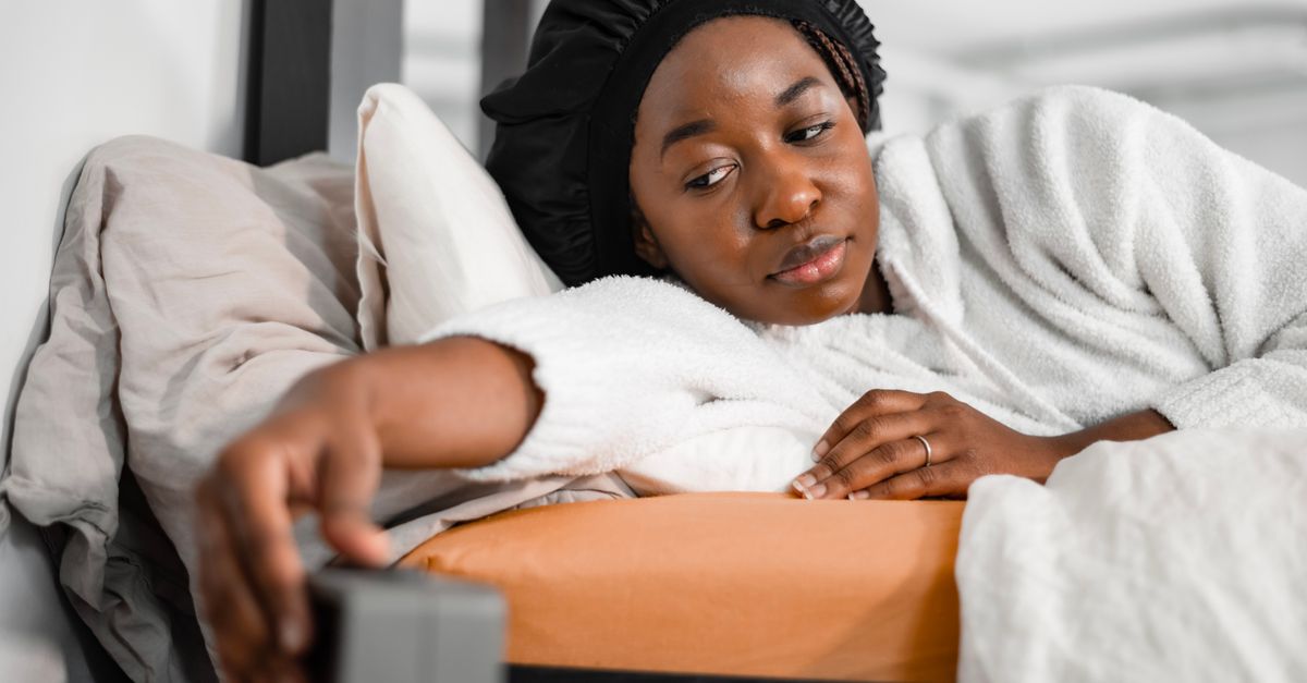 Woman in a robe lying in bed reaching for her alarm clock in the morning