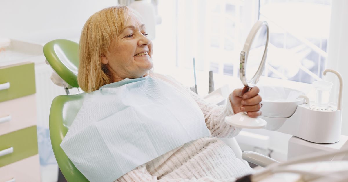 Smiling woman in a dental chair looking at her teeth in a hand mirror