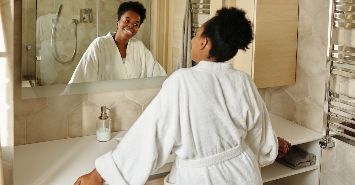 Woman in a bathrobe smiling at her reflection in a bathroom mirror