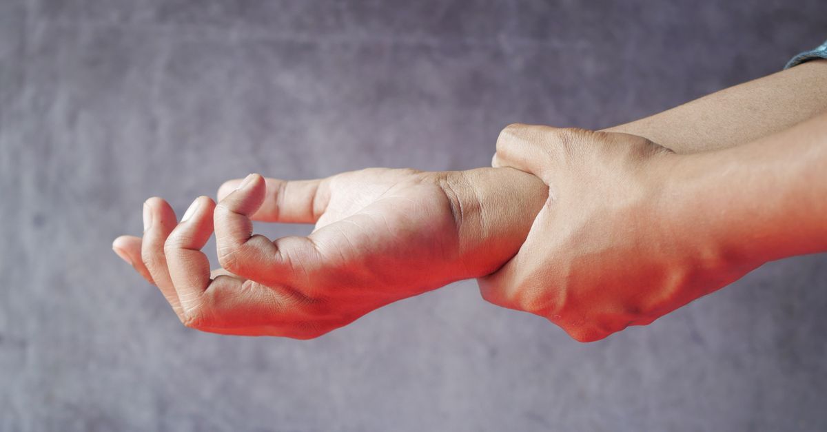 Hand holding a sore wrist against a gray background