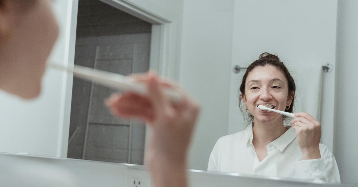 Woman brushing her teeth and looking in a bathroom mirror at home