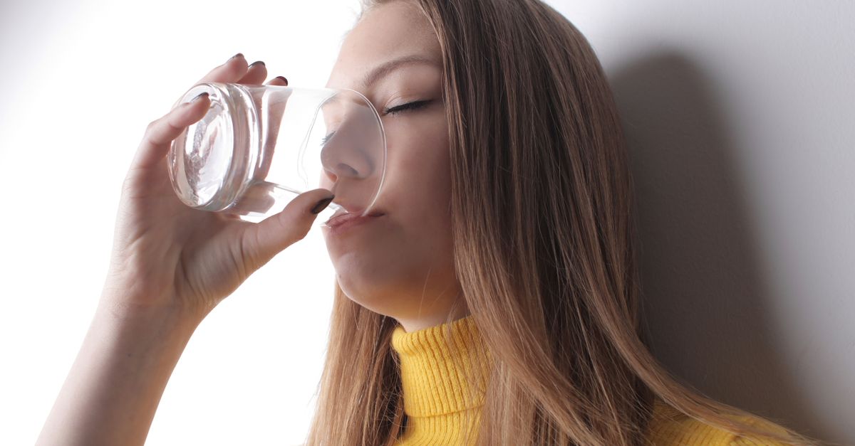 Woman in a yellow sweater drinking a glass of water