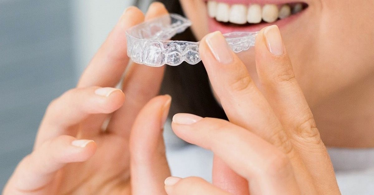 Woman holding a clear aligner in front of her smile