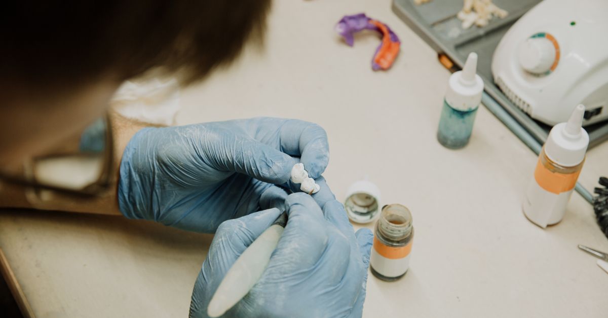 Dental lab technician in gloves shaping a single tooth restoration at a workbench