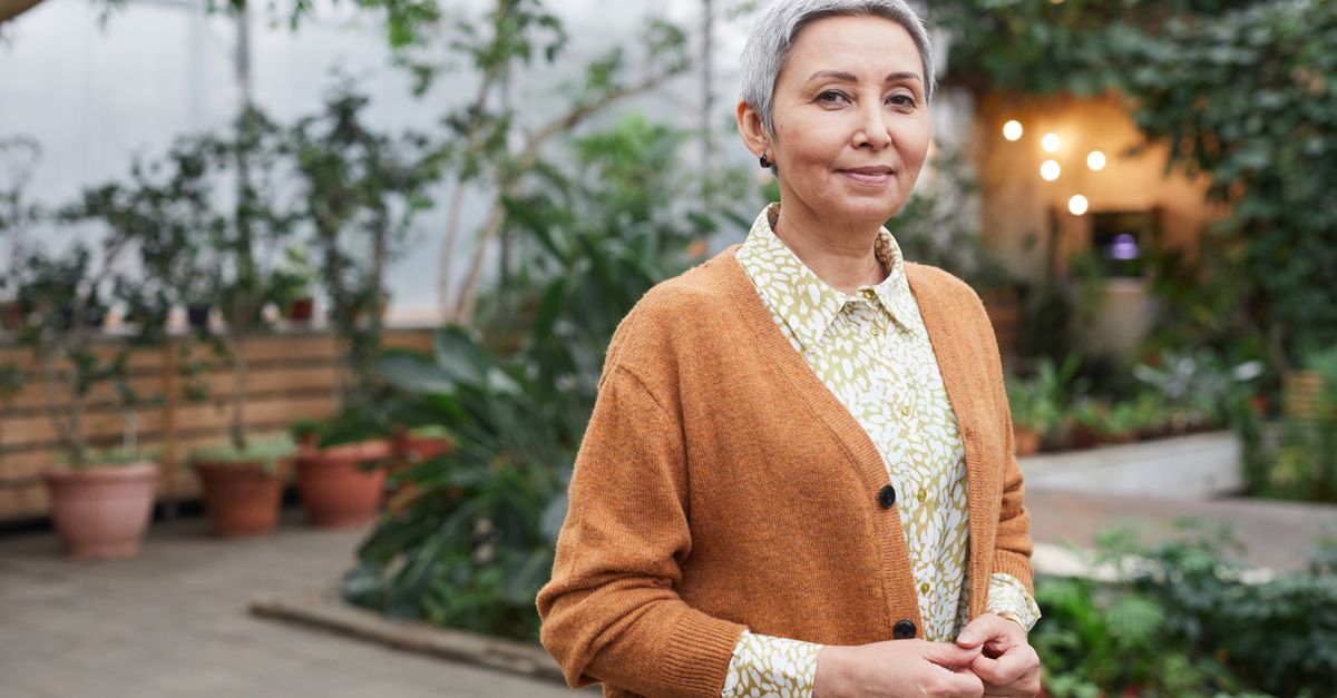 Older woman in a cardigan smiling calmly in a greenhouse
