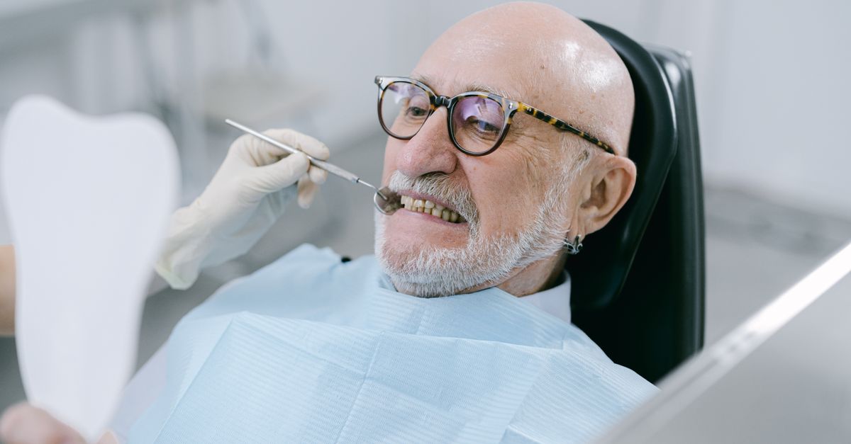 Older man in glasses during a dental exam, holding a hand mirror
