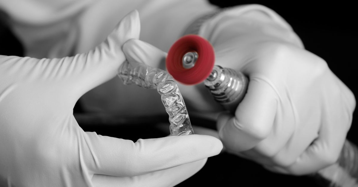 Gloved hands finishing the edge of a clear aligner in a dental lab
