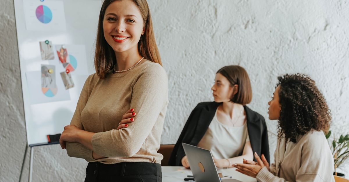 Smiling woman standing in an office meeting with colleagues at a table behind her