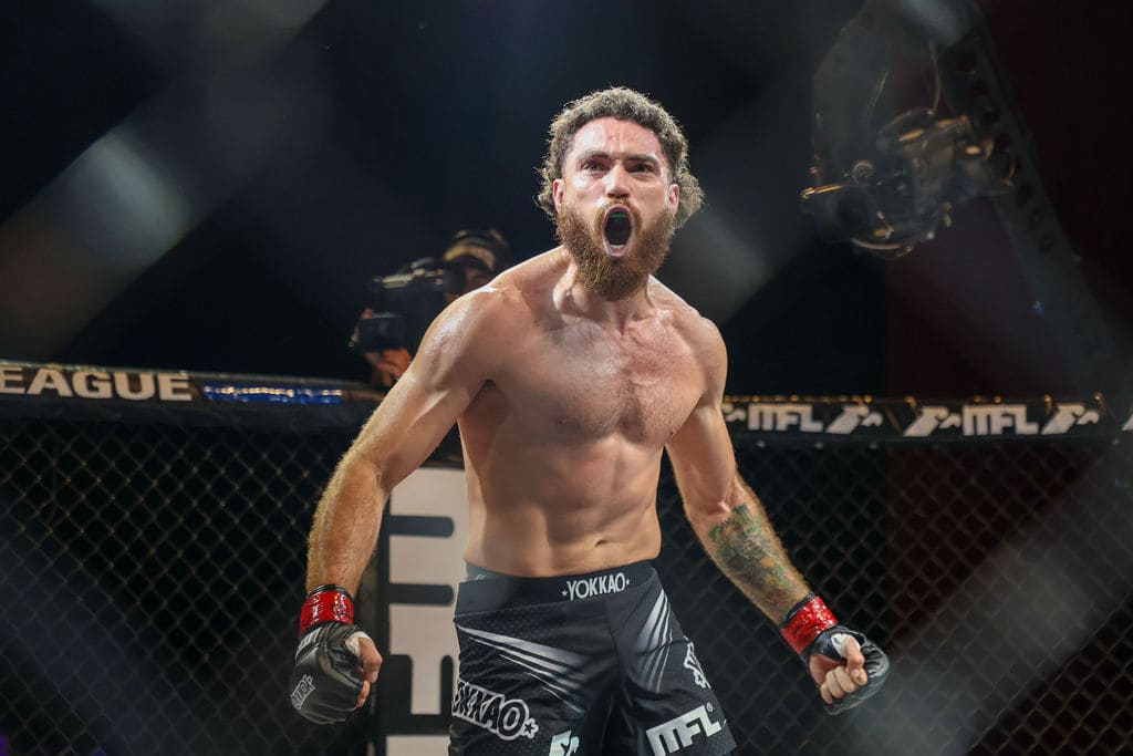 Luchador de MMA sin camisa gritando dentro del octágono con guantes de combate.