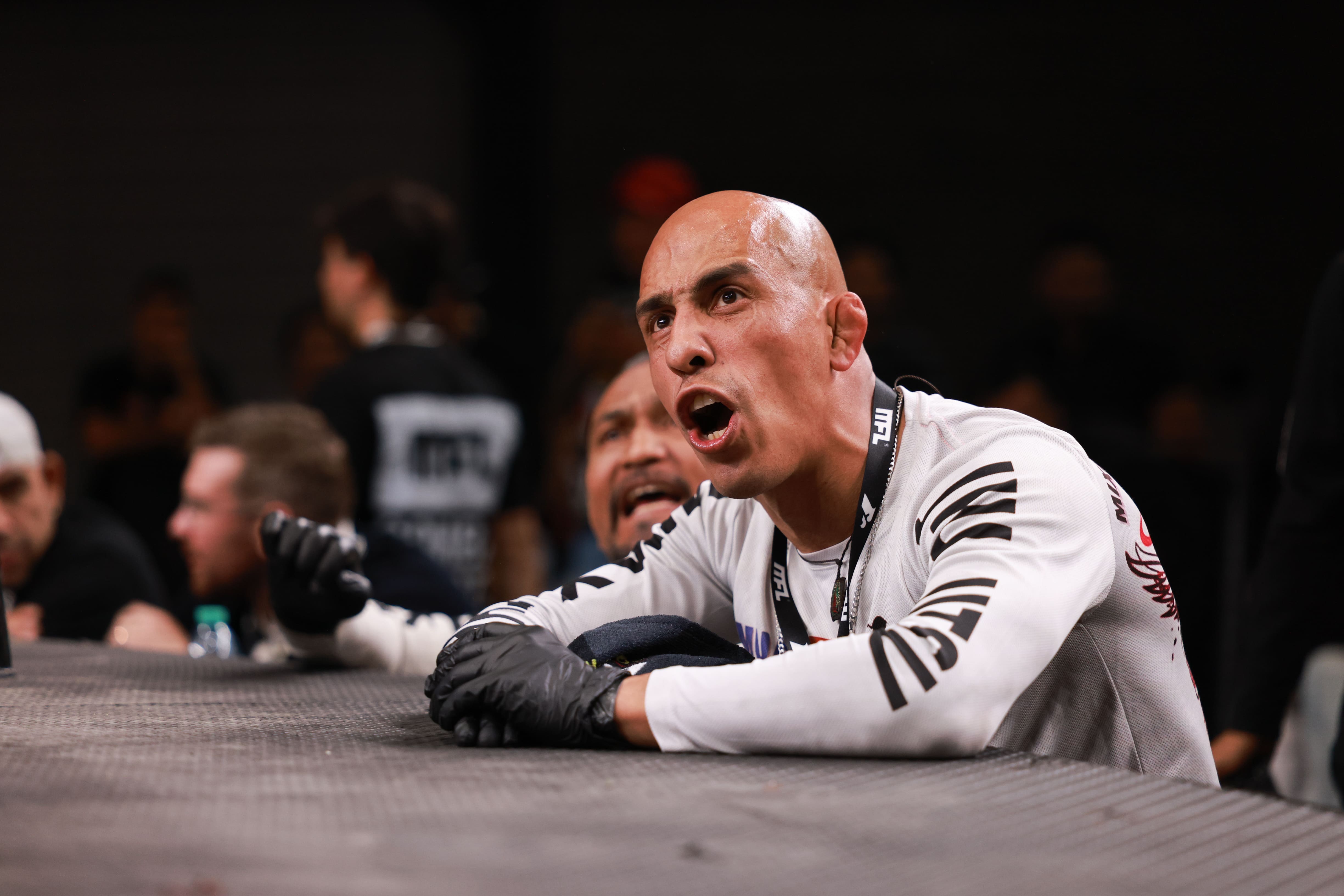 Hombre calvo con guantes negros gritando apoyado en la jaula de una pelea de MMA.