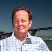 A man with long hair wearing a black jacket stands confidently, showcasing a stylish and modern appearance.
