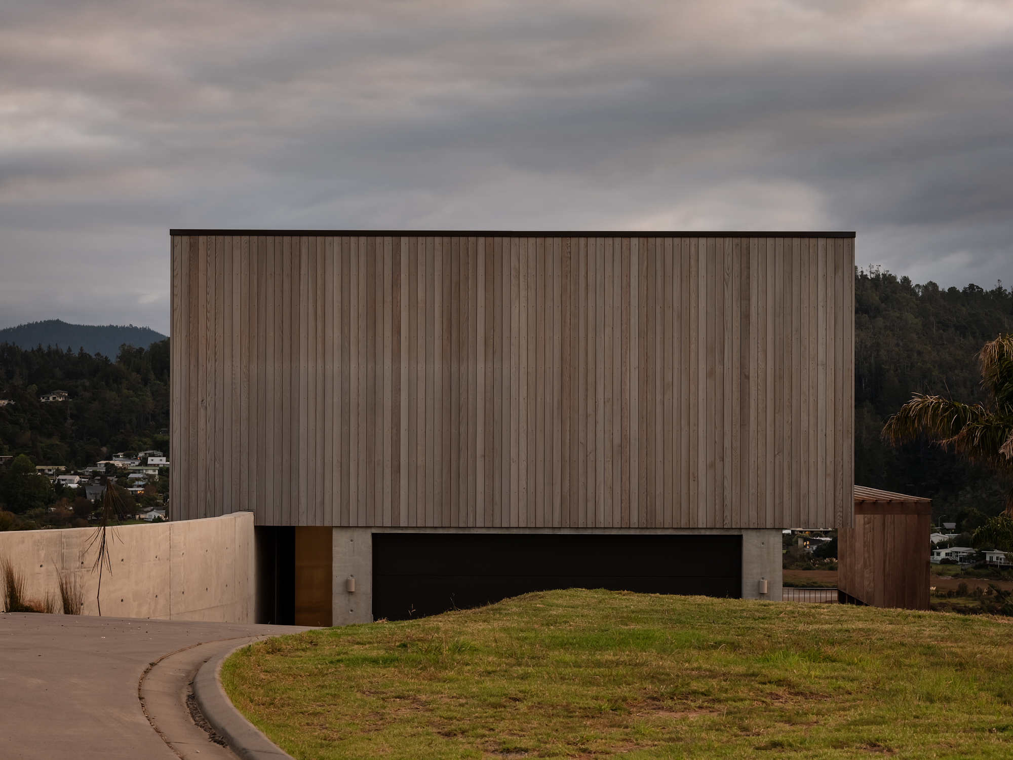 Cantilever House by Matt Deeb Architecture: Modern house with vertical wooden cedar paneling, concrete base, and a hilly grassy front entrance.